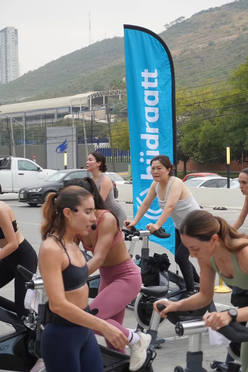 Ciclistas de spinning al aire libre junto a una bandera de Hudraatt