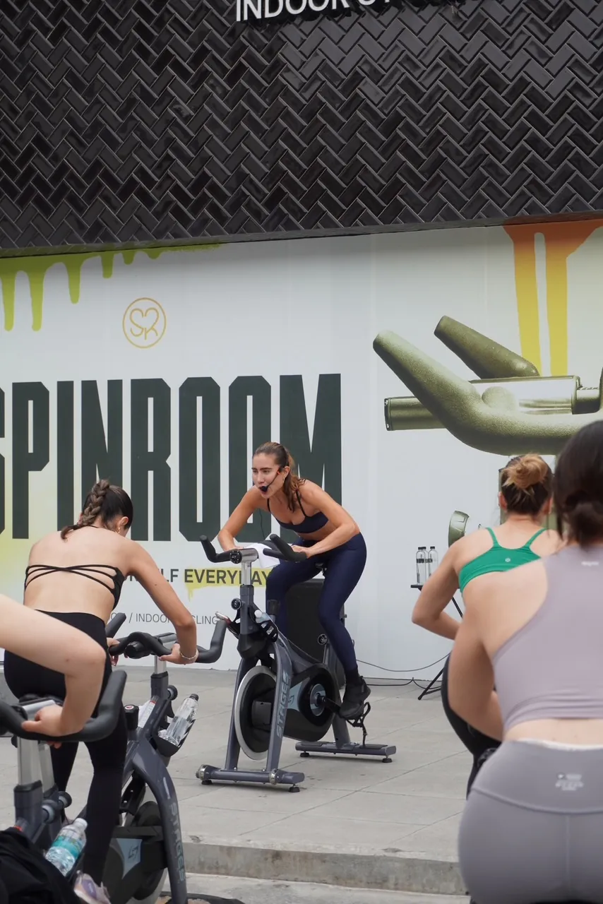 Mujeres pedaleando en una clase de spinning al aire libre frente al mural de Spinroom