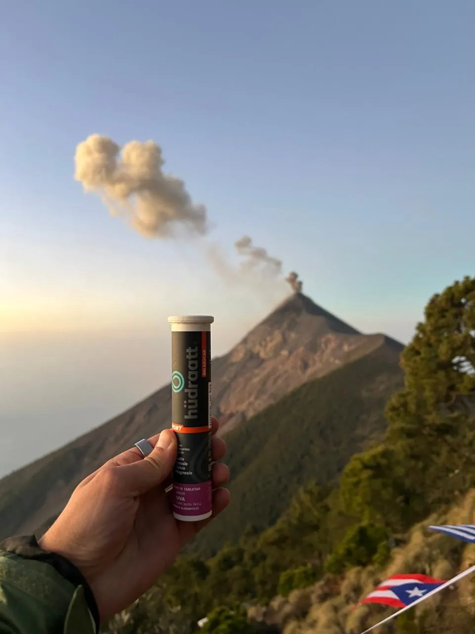 Mano sosteniendo un tubo de Hudraatt frente a un volcán con una fumarola