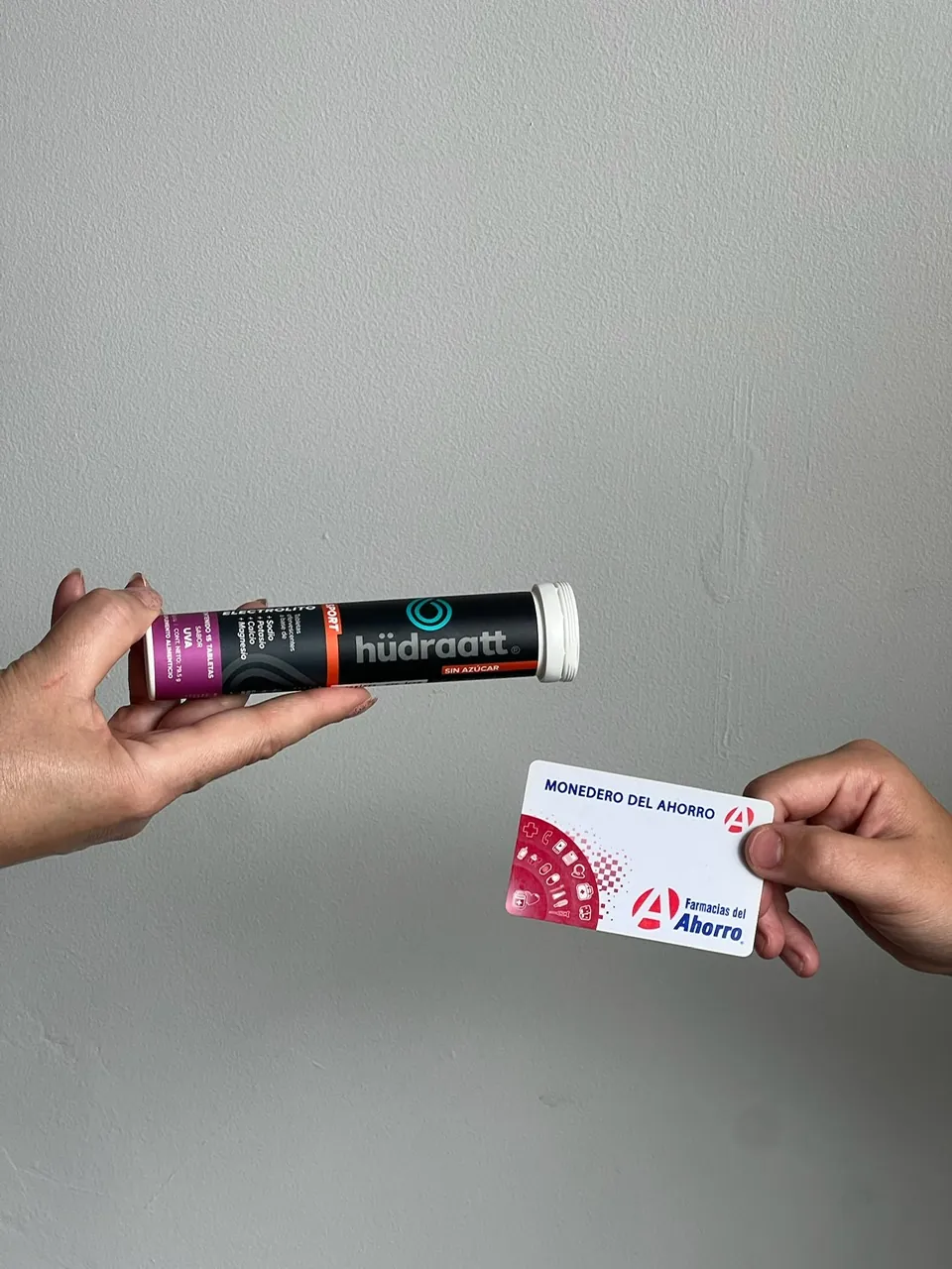 Una mano con un tubo de Hudraatt Uva y otra con una tarjeta Monedero del Ahorro