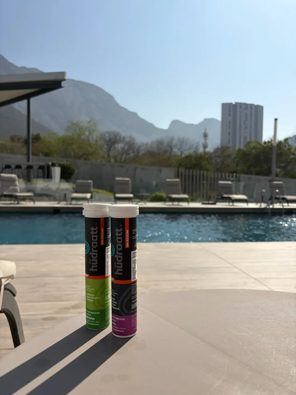 Tubos de Hudraatt Uva y Manzana junto a una alberca con montañas al fondo