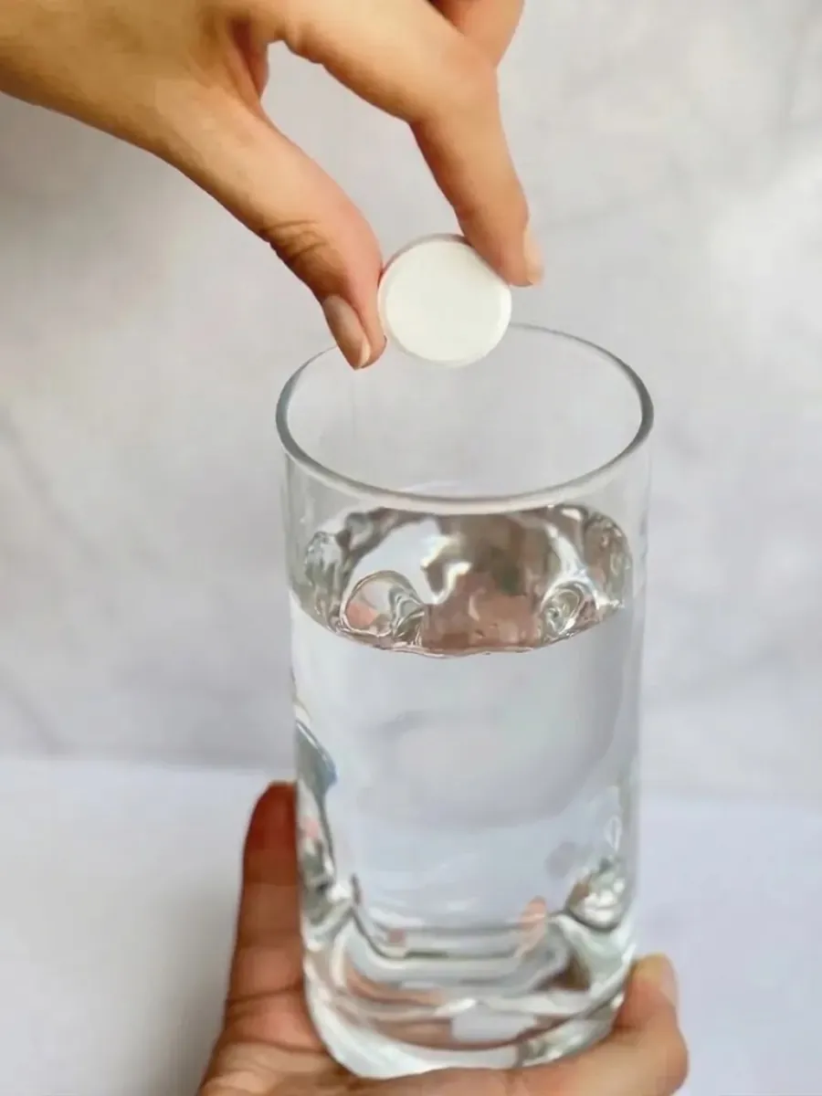 Una tableta efervescente blanca, sin colorantes, cayendo en un vaso de agua transparente